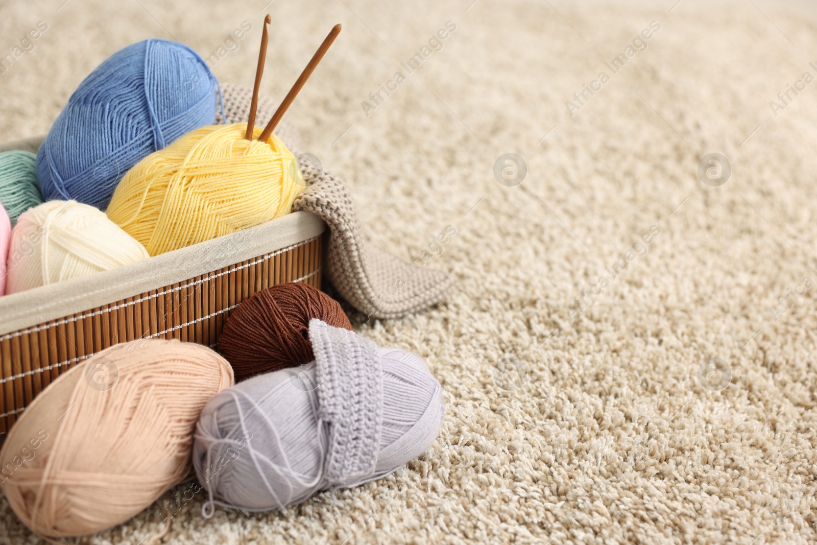 Photo of Colorful yarns, crochet sample, hooks and basket on soft carpet, closeup. Space for text