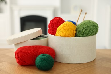 Boxes with colorful yarns and knitting needles on wooden table indoors, closeup