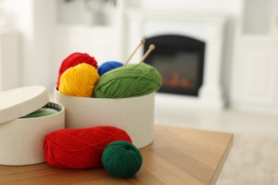 Boxes with colorful yarns and knitting needles on wooden table indoors. Space for text