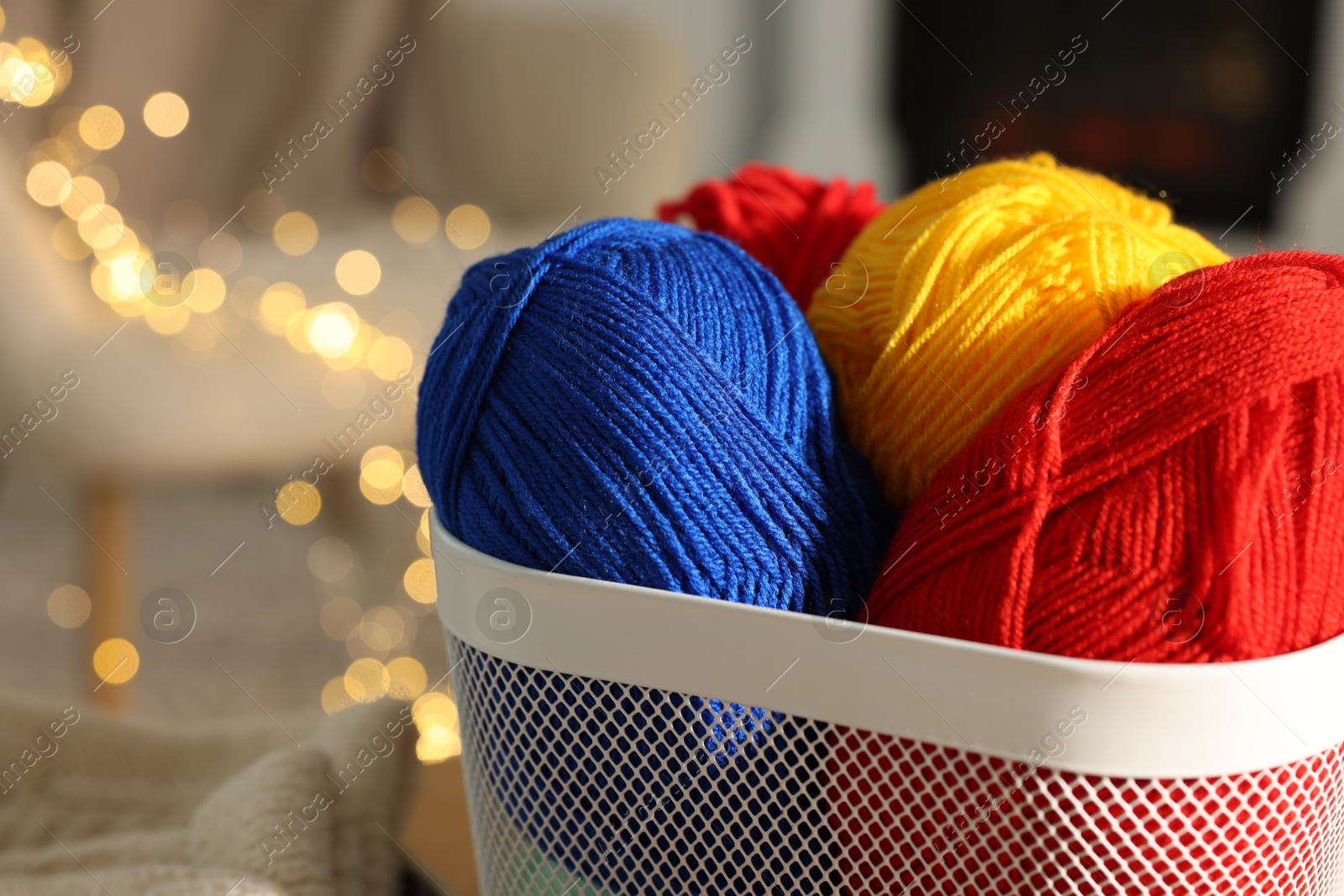 Photo of Colorful yarns in basket against blurred lights, closeup