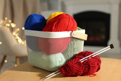 Colorful yarns, knitting needles, pattern sample and basket on wooden table indoors, closeup