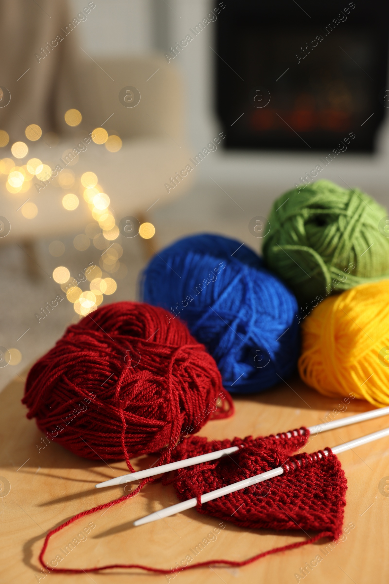 Photo of Colorful yarns, knitting needles and pattern sample on wooden table indoors, closeup