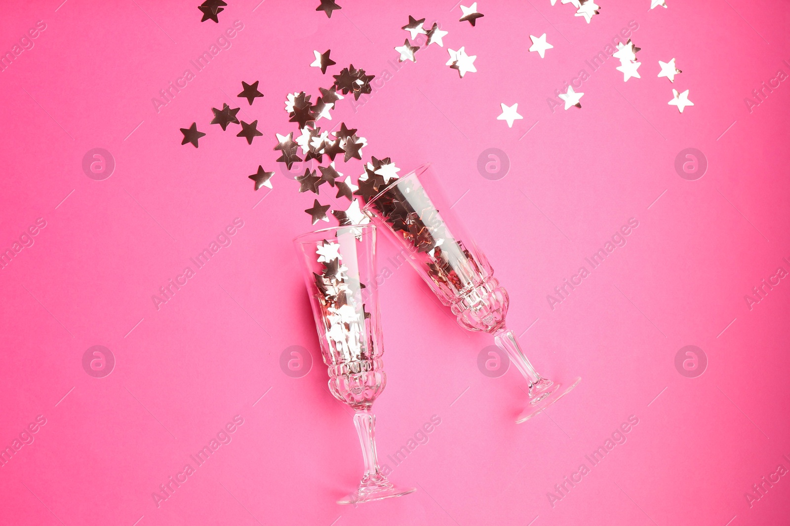 Photo of Wine glasses with confetti on pink background, flat lay. Christmas decor