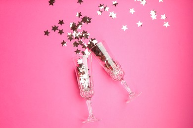 Photo of Wine glasses with confetti on pink background, flat lay. Christmas decor