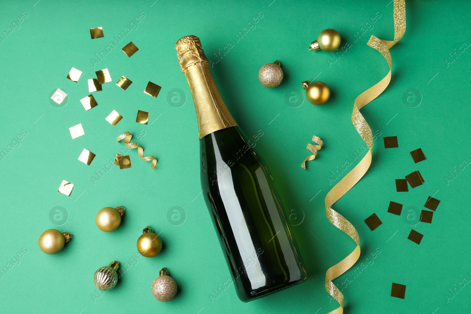 Photo of Bottle of sparkling wine, confetti and Christmas balls on green background, flat lay