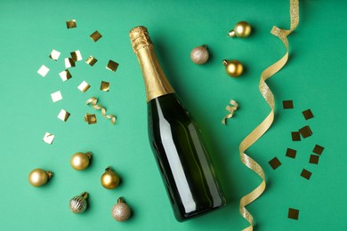 Photo of Bottle of sparkling wine, confetti and Christmas balls on green background, flat lay