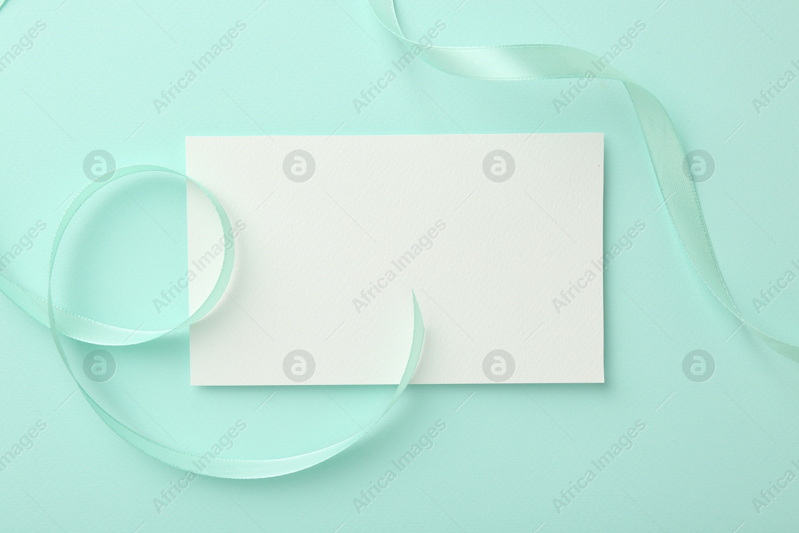 Photo of Blank card and ribbon on turquoise background, top view