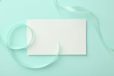 Photo of Blank card and ribbon on turquoise background, top view