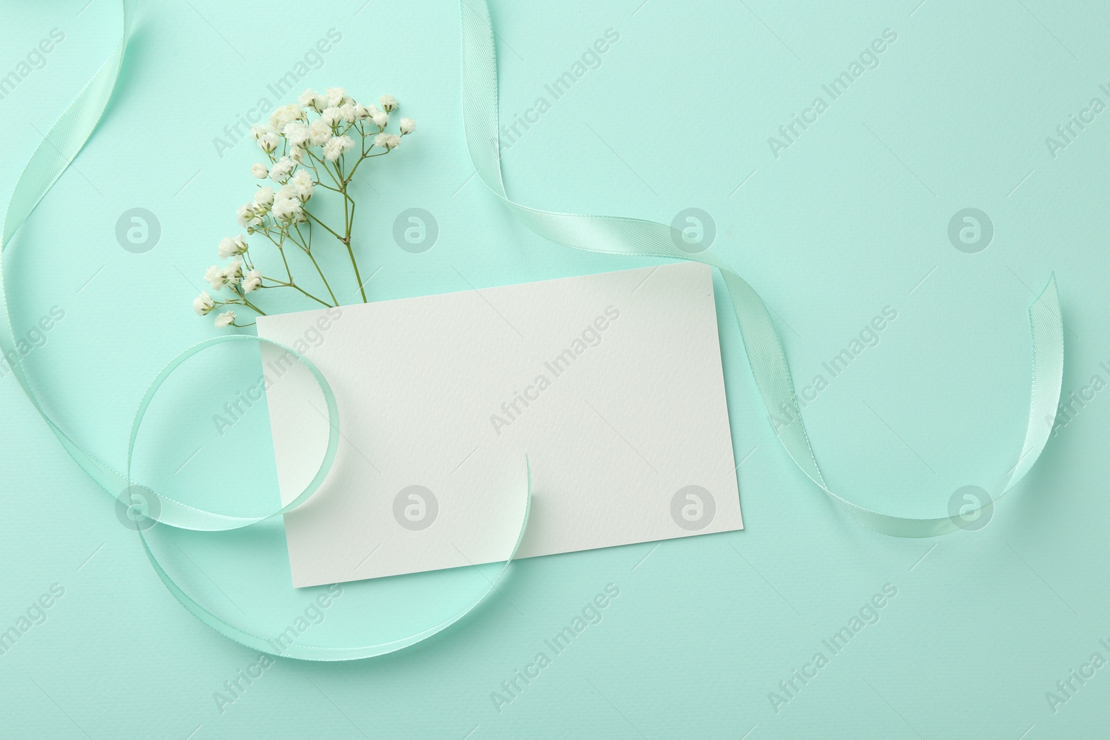 Photo of Flat lay composition with blank card, gypsophila flowers and ribbons on turquoise background