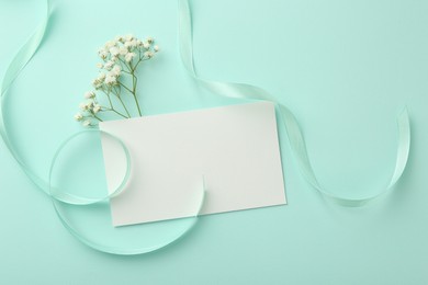 Flat lay composition with blank card, gypsophila flowers and ribbons on turquoise background