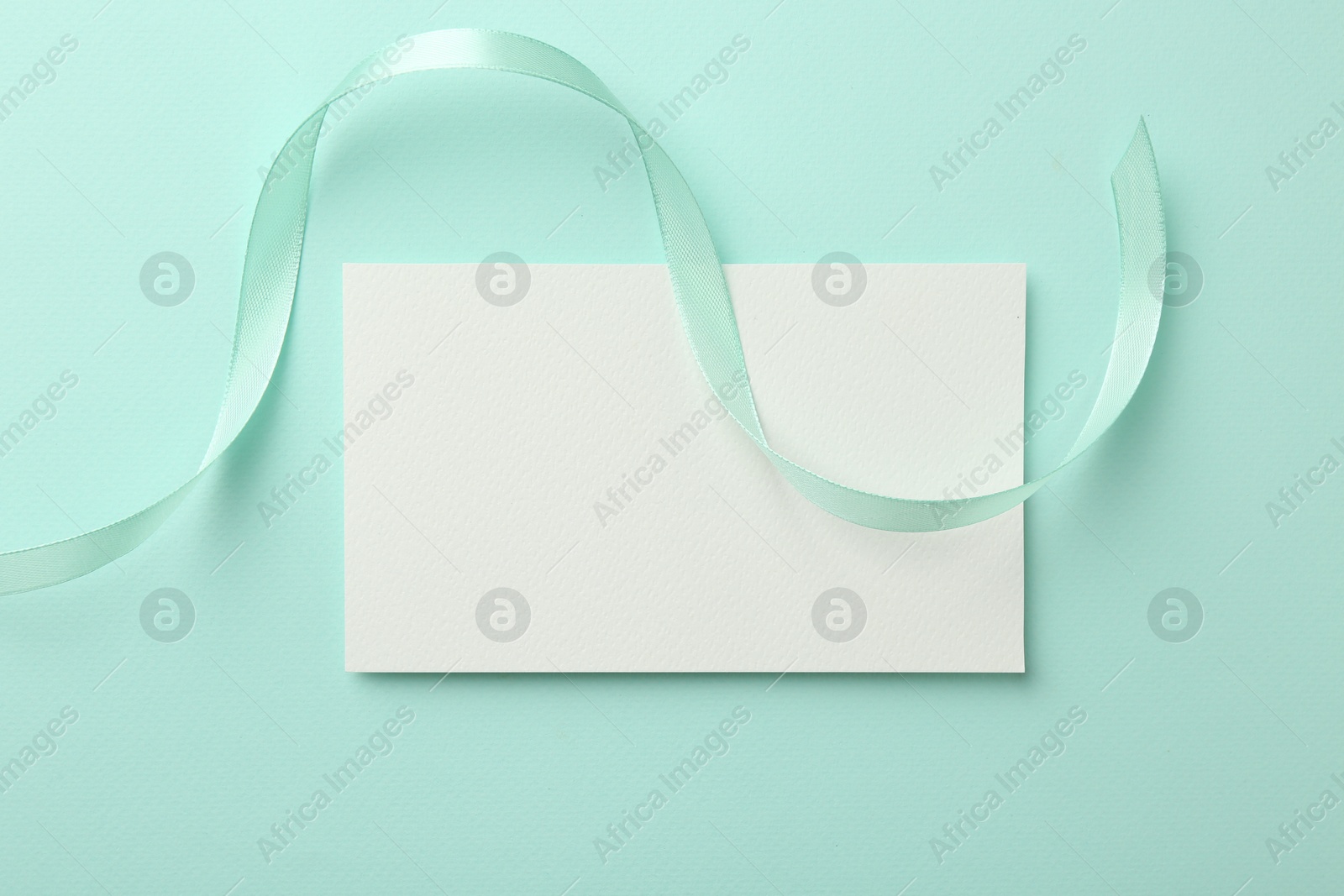 Photo of Blank card and ribbon on turquoise background, top view