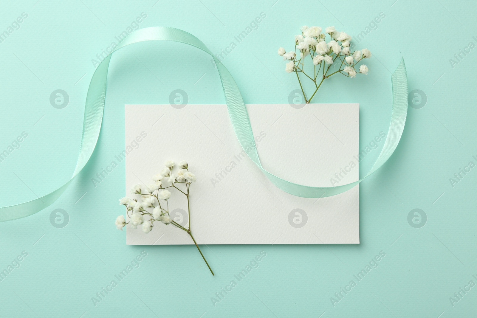 Photo of Flat lay composition with blank card, gypsophila flowers and ribbons on turquoise background