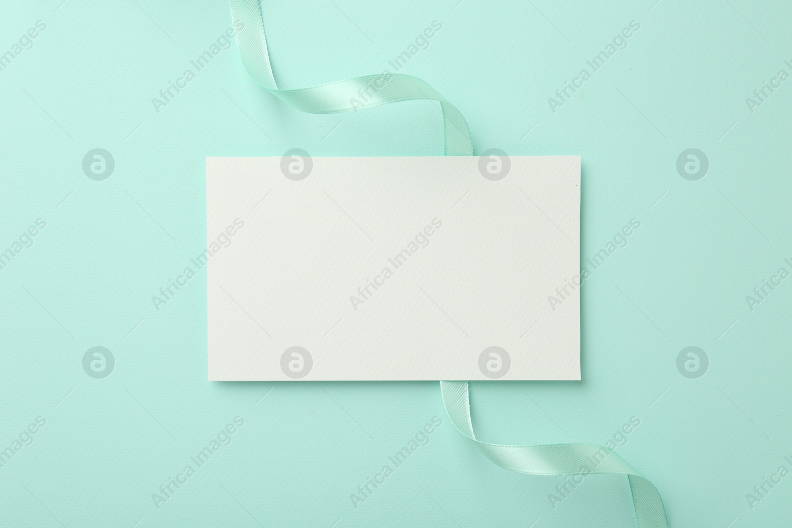 Photo of Blank card and ribbon on turquoise background, top view