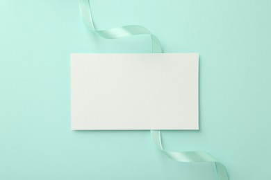 Photo of Blank card and ribbon on turquoise background, top view