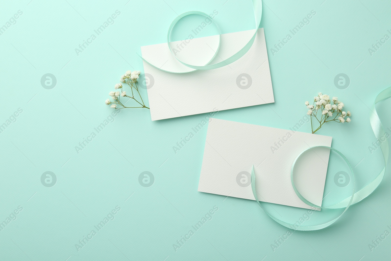 Photo of Flat lay composition with blank card, gypsophila flowers and ribbons on turquoise background. Space for text