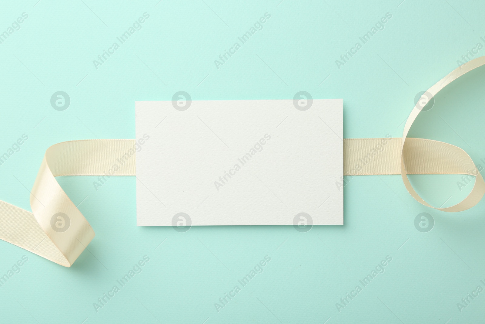 Photo of Blank card and ribbon on turquoise background, top view