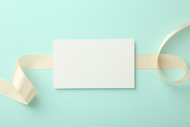 Blank card and ribbon on turquoise background, top view