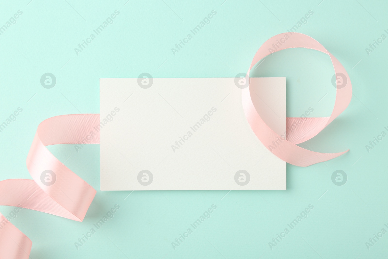 Photo of Blank card and ribbon on turquoise background, top view