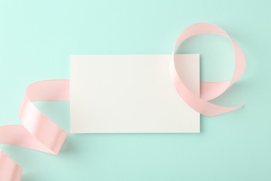 Blank card and ribbon on turquoise background, top view