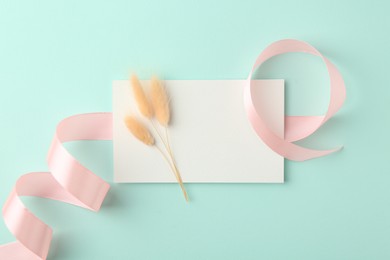 Blank card, spikelets and ribbon on turquoise background, top view