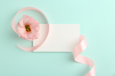 Blank card, flower and ribbon on turquoise background, top view