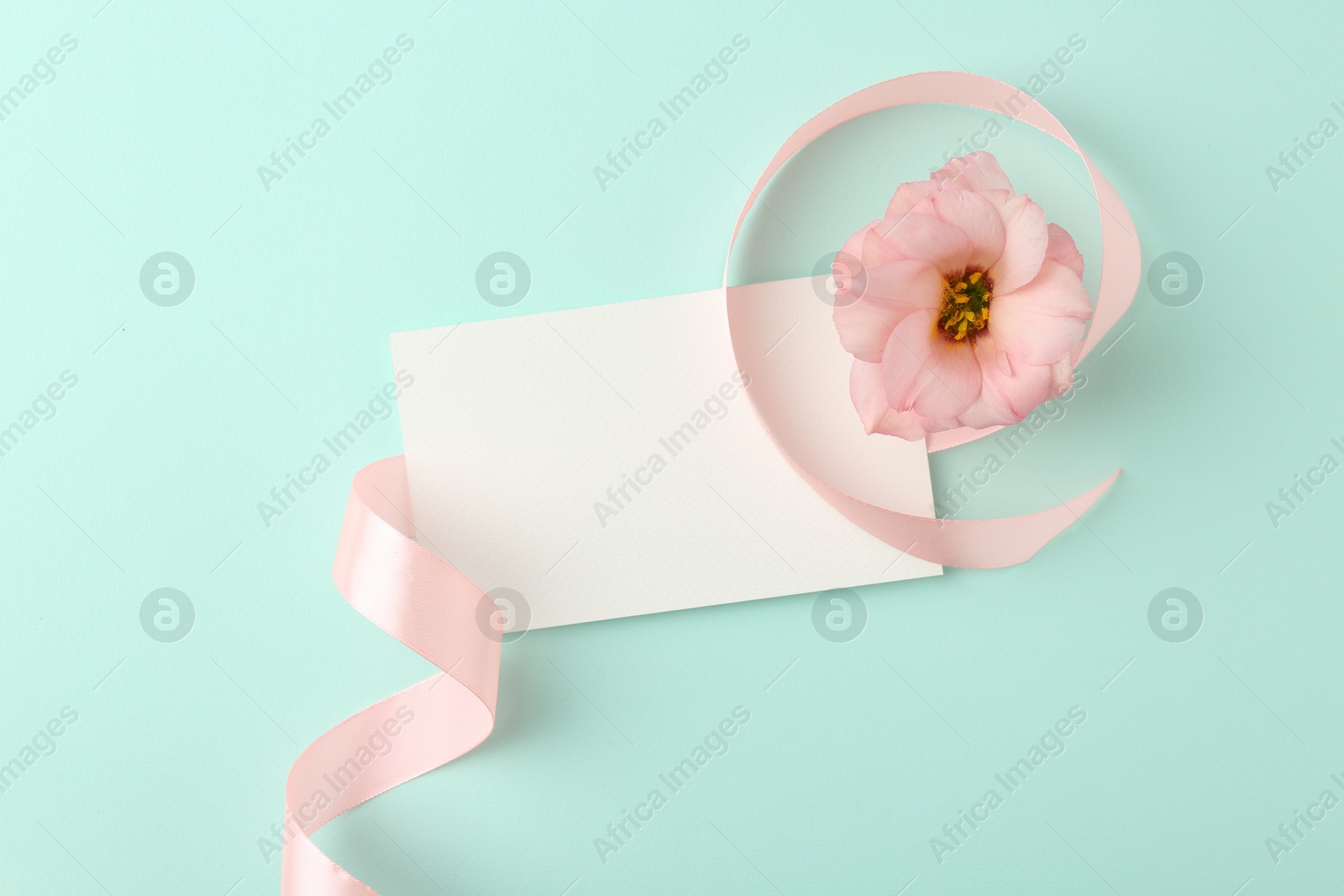 Photo of Blank card, flower and ribbon on turquoise background, top view