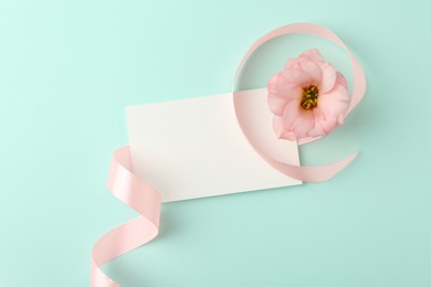 Blank card, flower and ribbon on turquoise background, top view