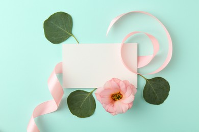 Blank card, flower, leaves and ribbon on turquoise background, flat lay