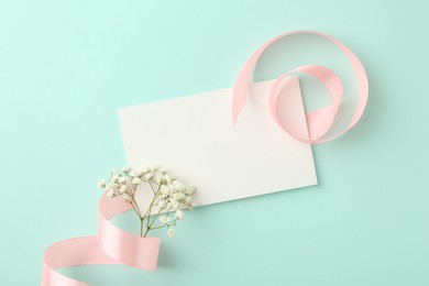 Flat lay composition with blank card, gypsophila flowers and ribbons on turquoise background