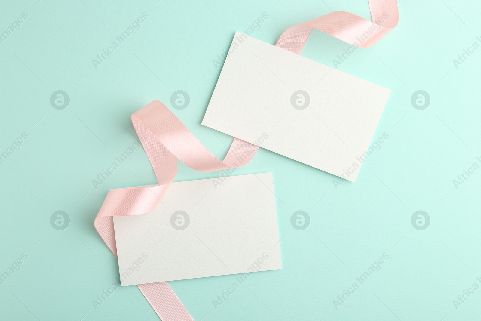 Photo of Blank cards and ribbons on turquoise background, flat lay