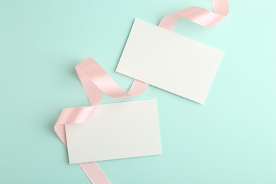 Photo of Blank cards and ribbons on turquoise background, flat lay