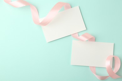 Photo of Blank cards and ribbons on turquoise background, flat lay. Space for text