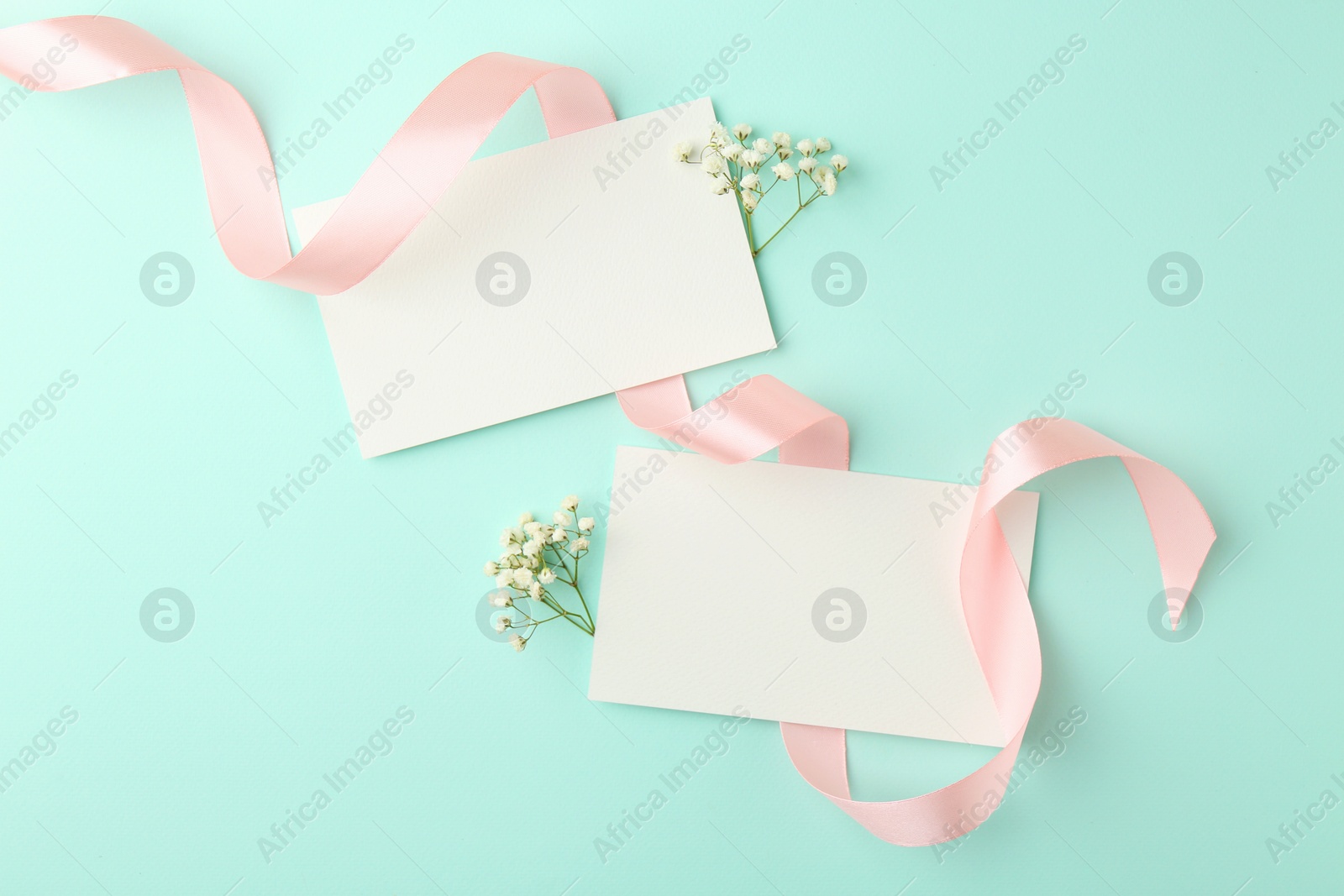 Photo of Flat lay composition with blank cards, gypsophila flowers and ribbon on turquoise background