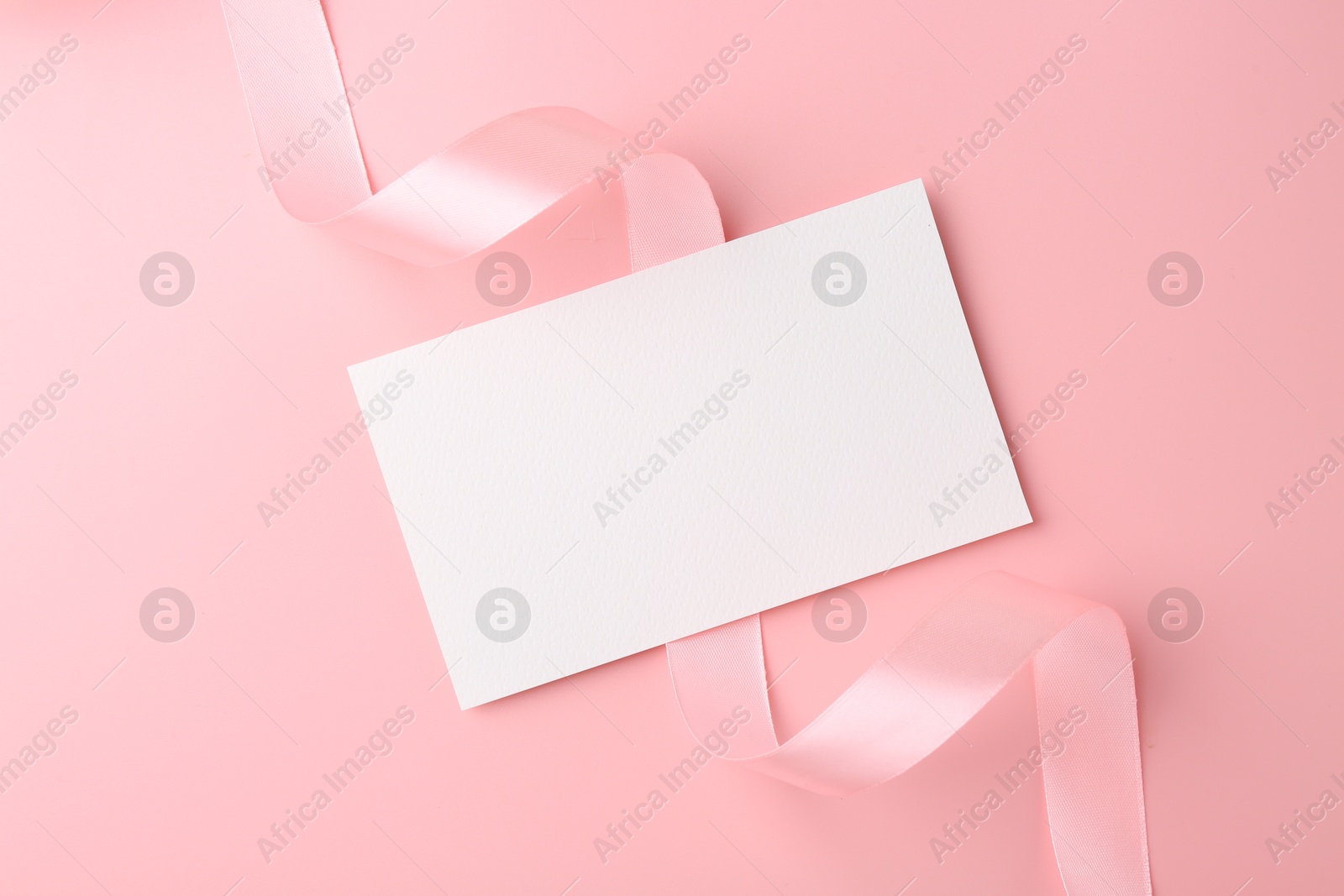 Photo of Blank card and ribbon on pink background, top view