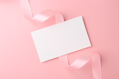 Photo of Blank card and ribbon on pink background, top view