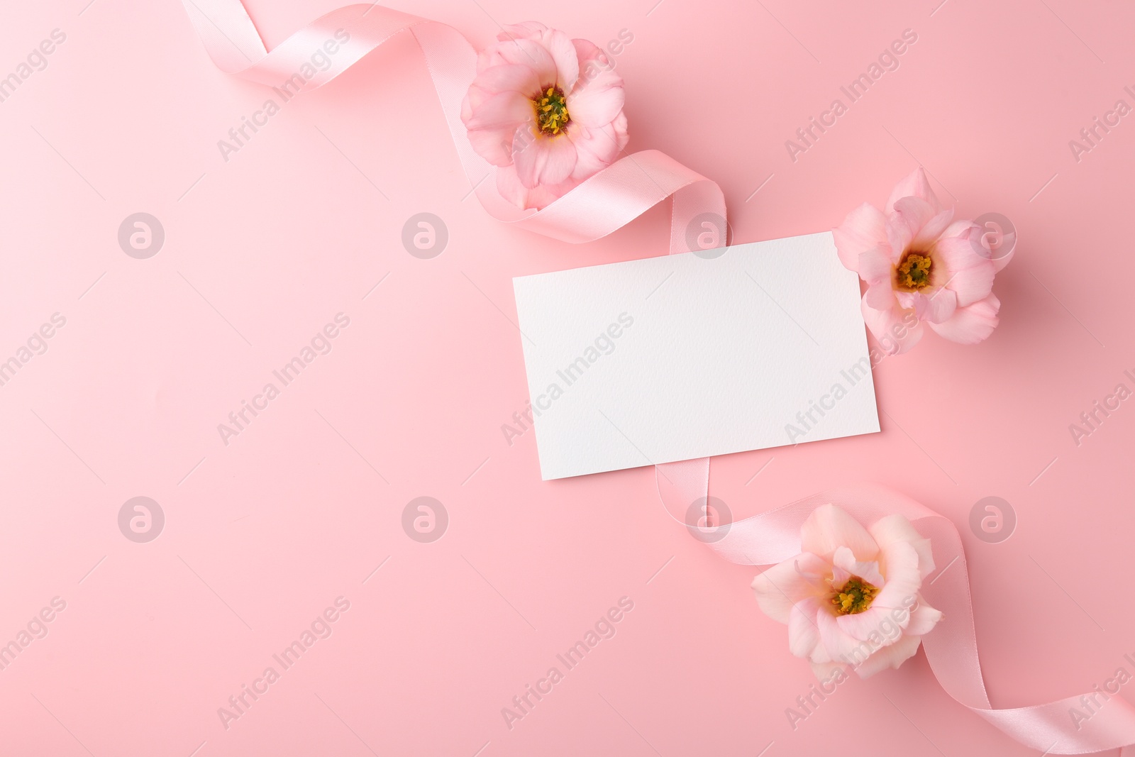 Photo of Flat lay composition with blank card, flowers and ribbons on pink background. Space for text