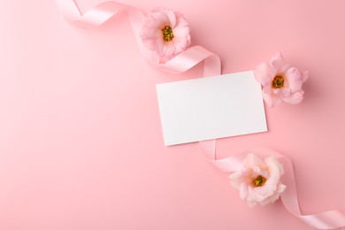 Flat lay composition with blank card, flowers and ribbons on pink background. Space for text