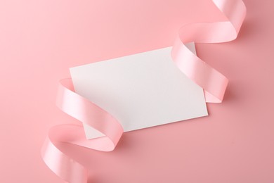 Blank card and ribbon on pink background, top view