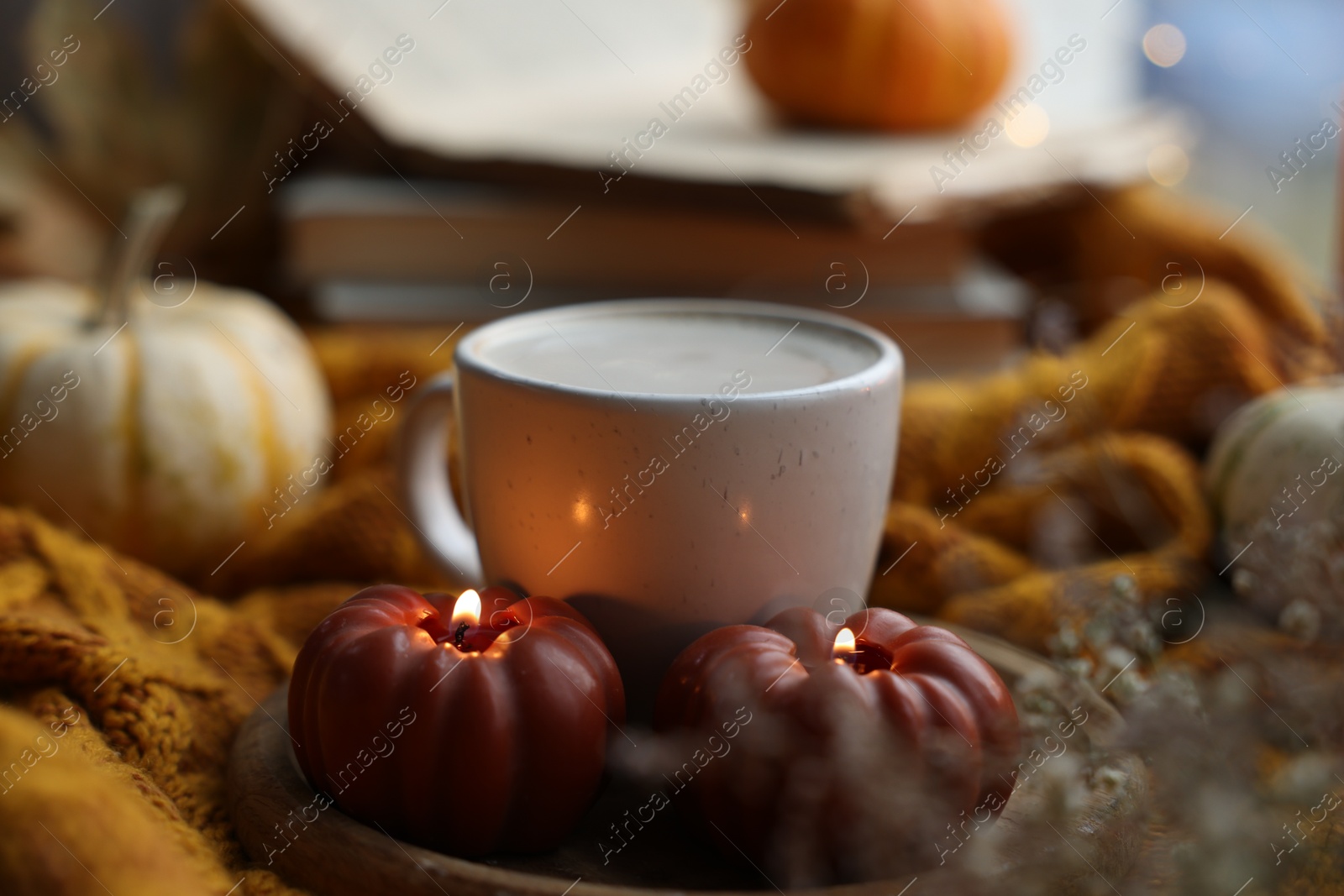 Photo of Cup of coffee and burning pumpkin shaped candles on soft sweater, closeup. Autumn atmosphere