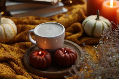 Photo of Cup of coffee and burning pumpkin shaped candles on soft sweater. Autumn atmosphere