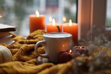 Photo of Cup of coffee and burning pumpkin shaped candles on soft sweater. Autumn atmosphere