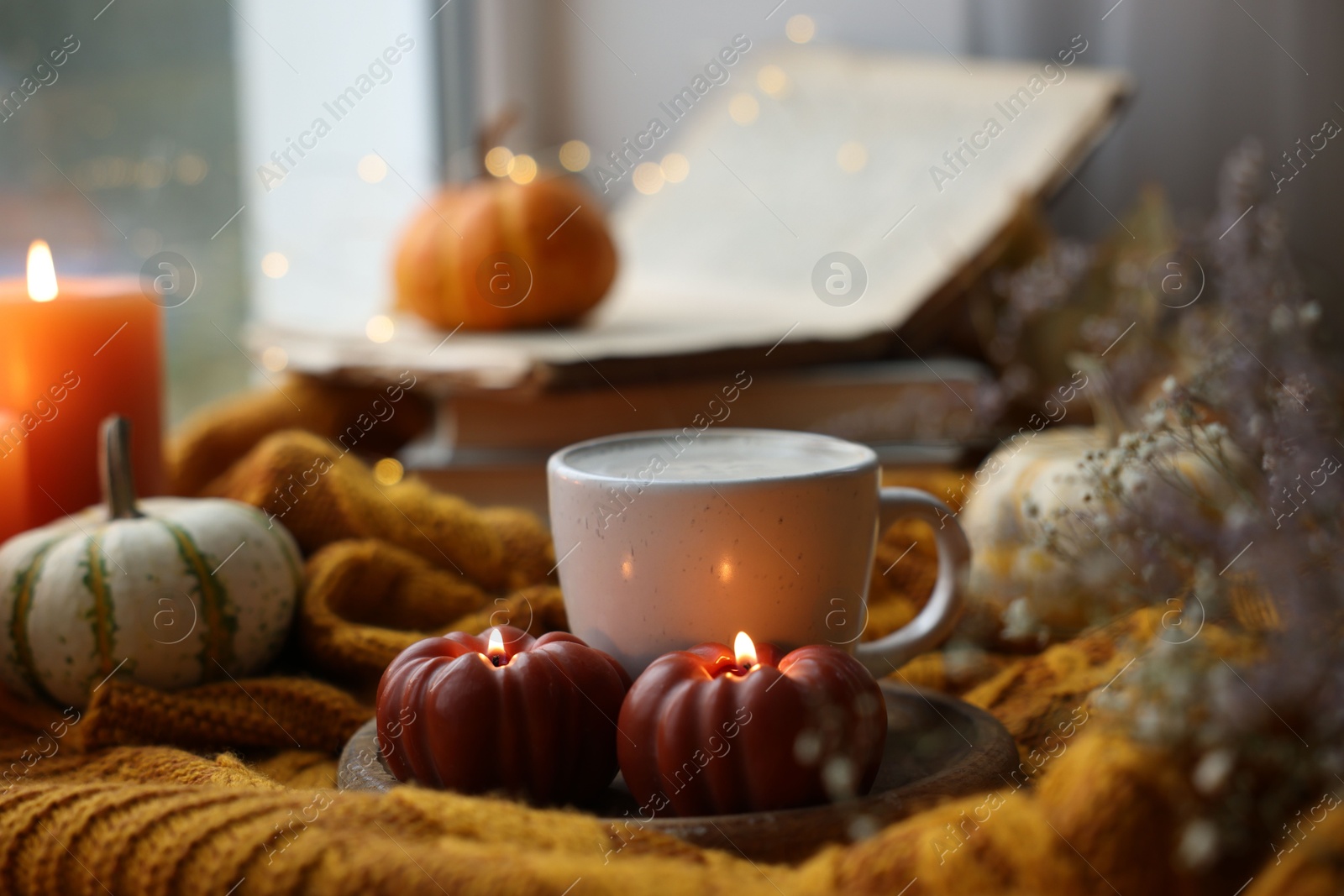 Photo of Cup of coffee and burning pumpkin shaped candles on soft sweater. Autumn atmosphere