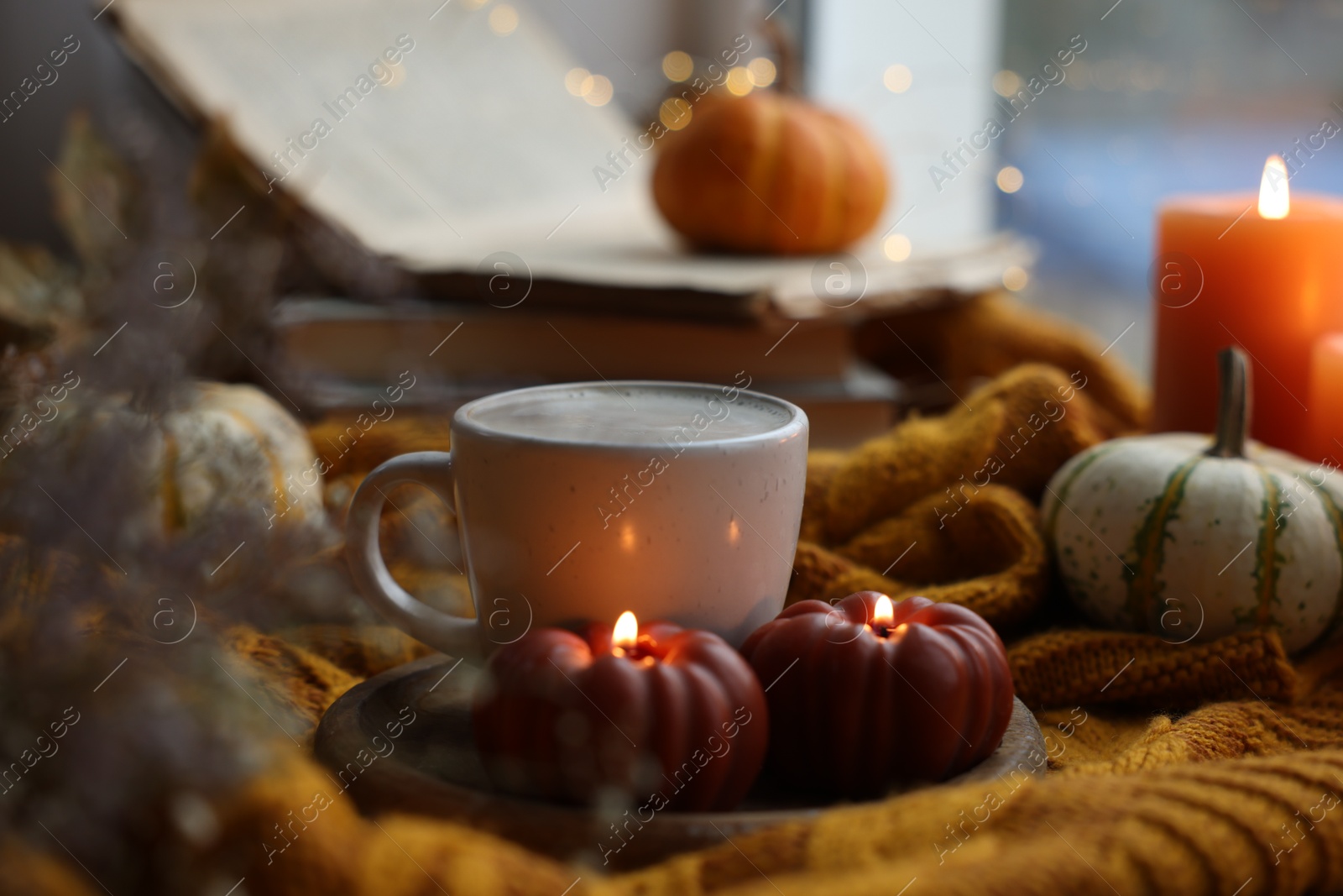 Photo of Cup of coffee and burning pumpkin shaped candles on soft sweater. Autumn atmosphere