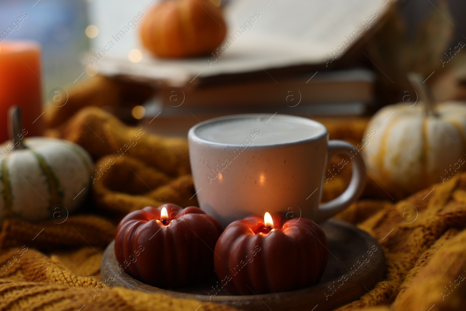 Photo of Cup of coffee and burning pumpkin shaped candles on soft sweater, closeup. Autumn atmosphere