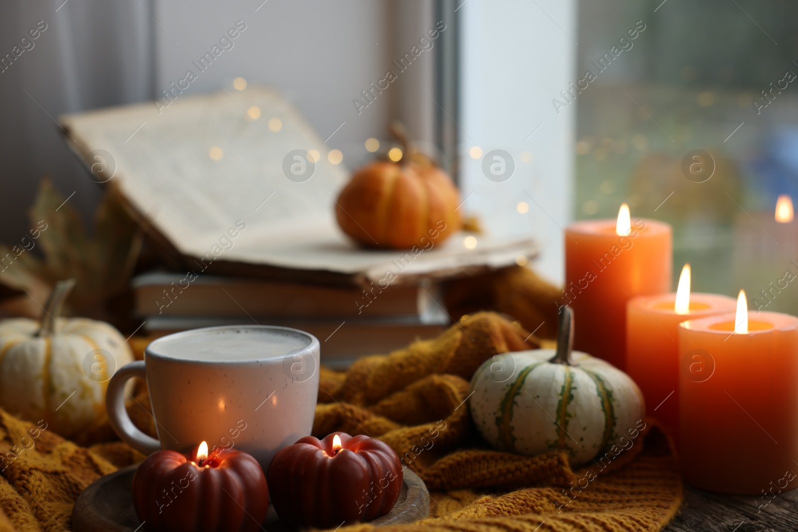 Photo of Cup of coffee, pumpkins, burning candles and soft sweater on table. Autumn atmosphere