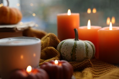 Photo of Cup of coffee, pumpkins and burning candles on soft sweater, closeup. Autumn atmosphere