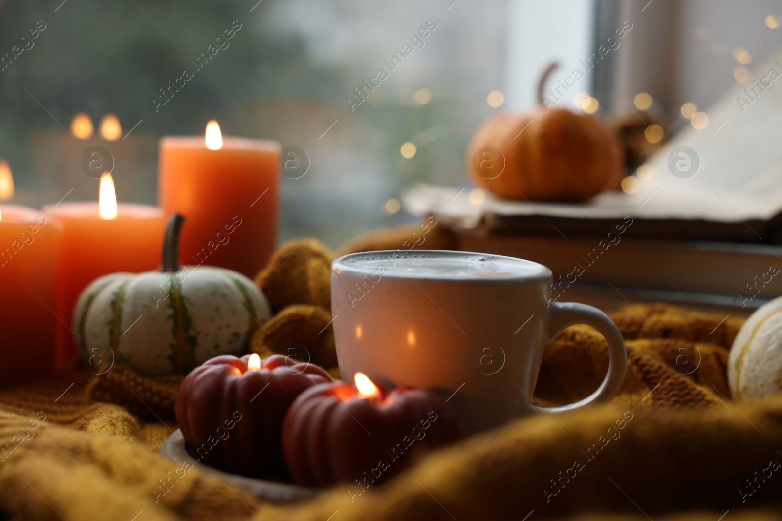 Photo of Cup of coffee, pumpkins and burning candles on soft sweater, closeup. Autumn atmosphere