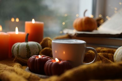 Photo of Cup of coffee, pumpkins and burning candles on soft sweater, closeup. Autumn atmosphere