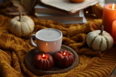 Photo of Cup of coffee, pumpkins, burning candles and soft sweater on table. Autumn atmosphere