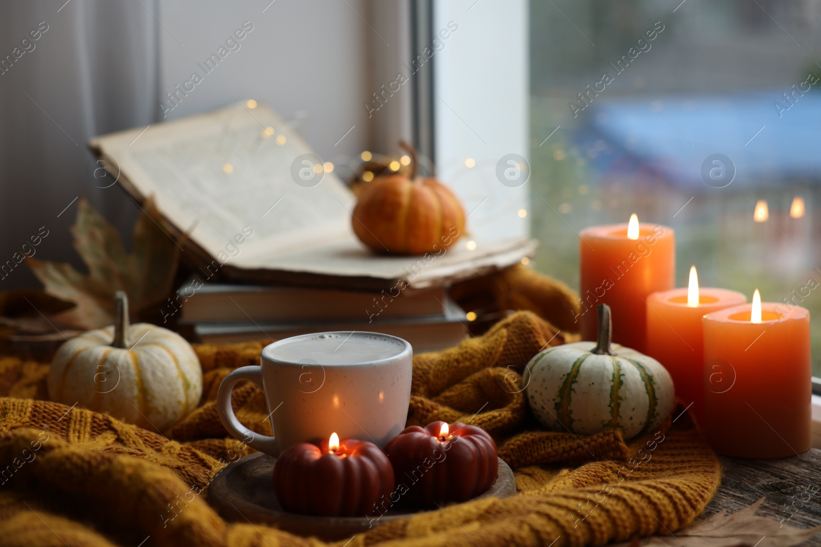 Photo of Cup of coffee, pumpkins, burning candles and soft sweater on table. Autumn atmosphere